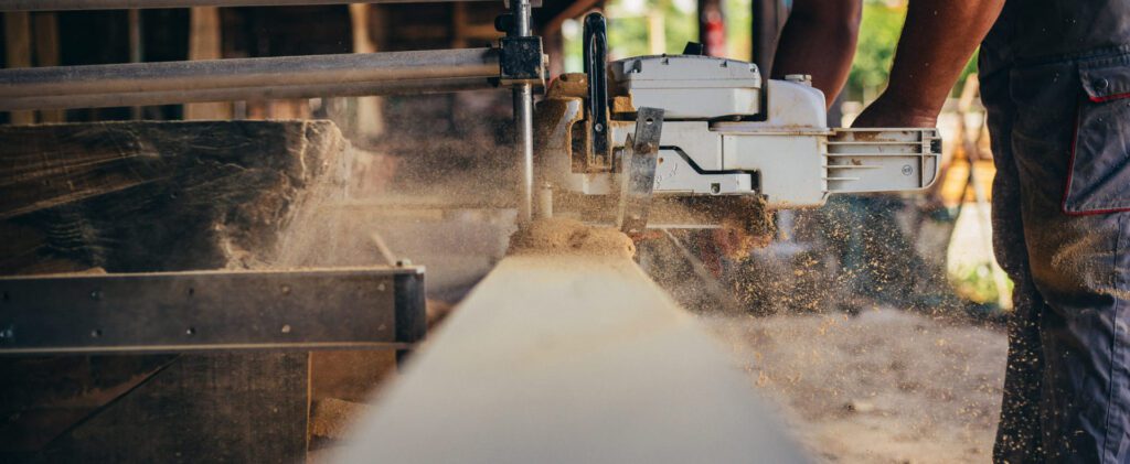 Woodworker operating a power saw to mill a thick plank of lumber, with sawdust spraying outward