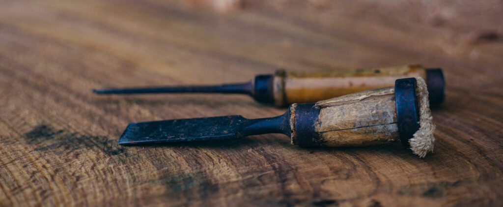 Two well-worn woodworking chisels lying on a richly grained oak plank.
