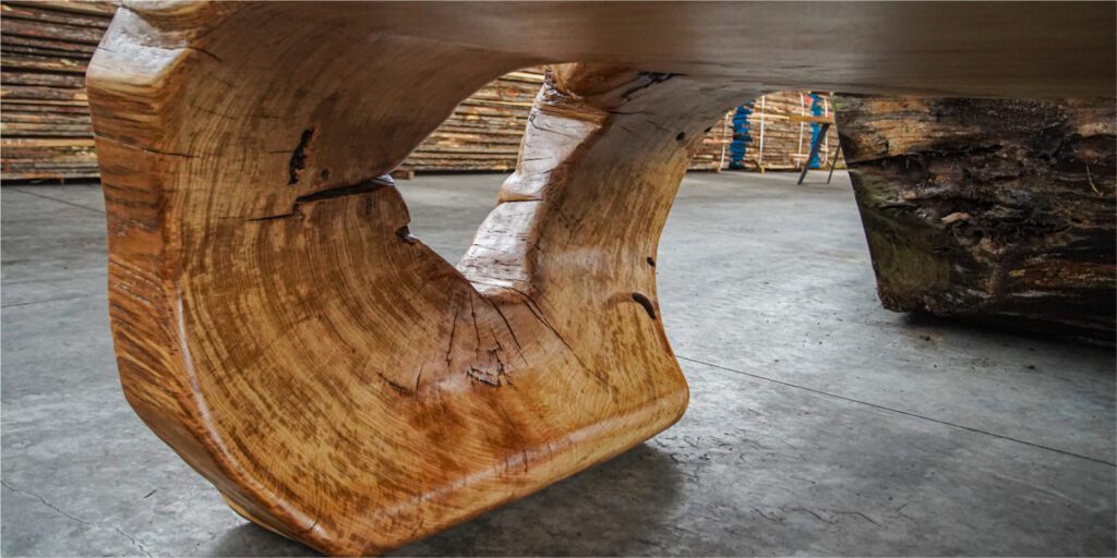 Close-up of Ragusa table’s live-edge base showing sculptural wood grain and natural cracks in workshop setting