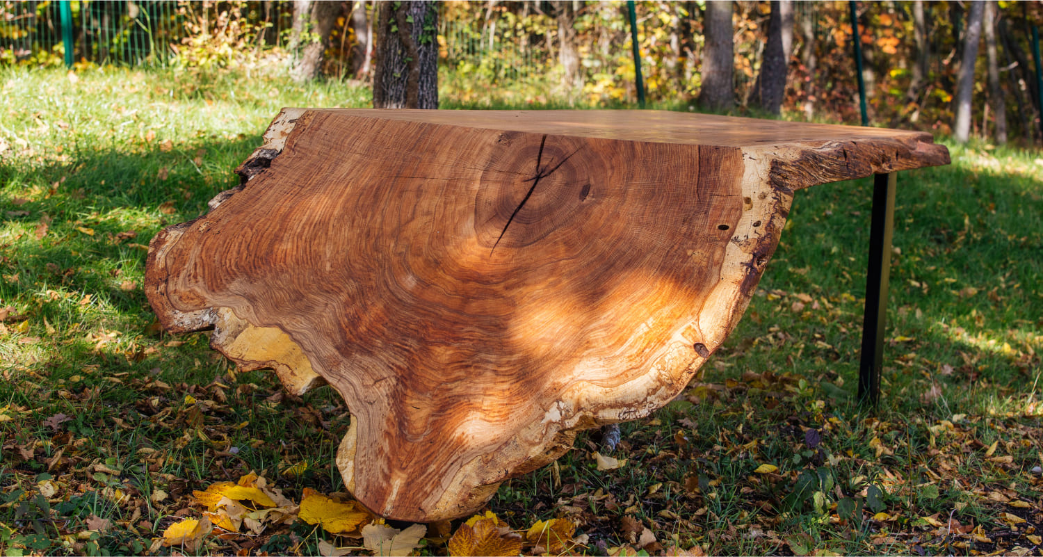 Close-up of Olea live-edge wooden table showing raw grain and natural edge in outdoor setting