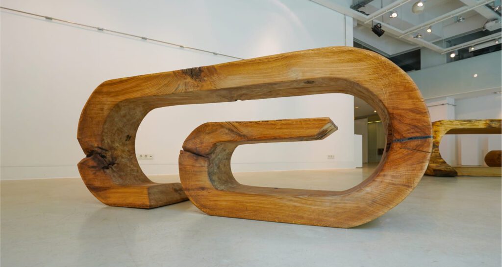 Side profile of sculptural OZE wooden commode showing continuous curved form and open space design in gallery