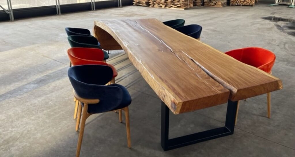 Ragusa solid wood table with live edge and colorful chairs in industrial workshop setting
