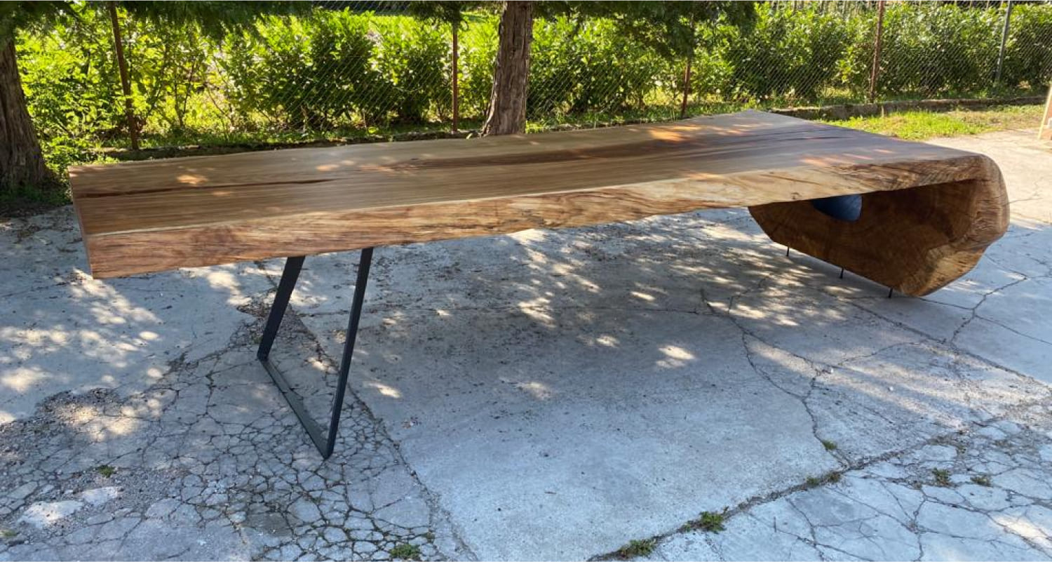 Ragusa oak wood table with sculpted base and live edge detail in outdoor stone setting