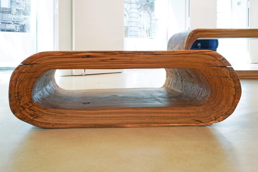 Front view of OZE sculptural wooden coffee table showing its seamless open-core design in a bright gallery