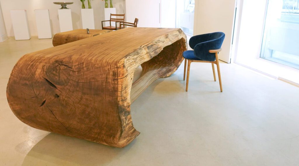 Side view of OZE sculptural wooden table end grain and live edge in a bright gallery